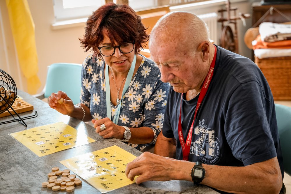 Zwei Bewohner spielen mit einer Betreuungskraft Bingo